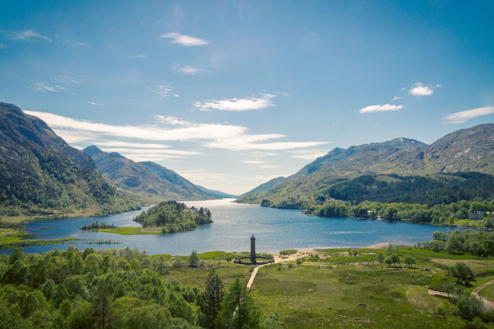 Scenic view of a lake with surrounding mountains and a small island with a tower.