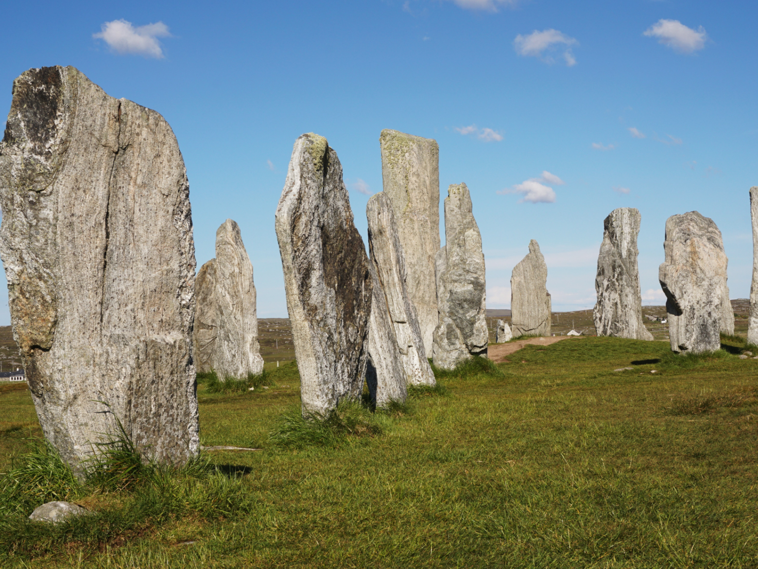 Stone monoliths standing upright in a grassy field under a blue sky.