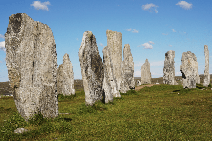 Stone monoliths standing upright in a grassy field under a blue sky.
