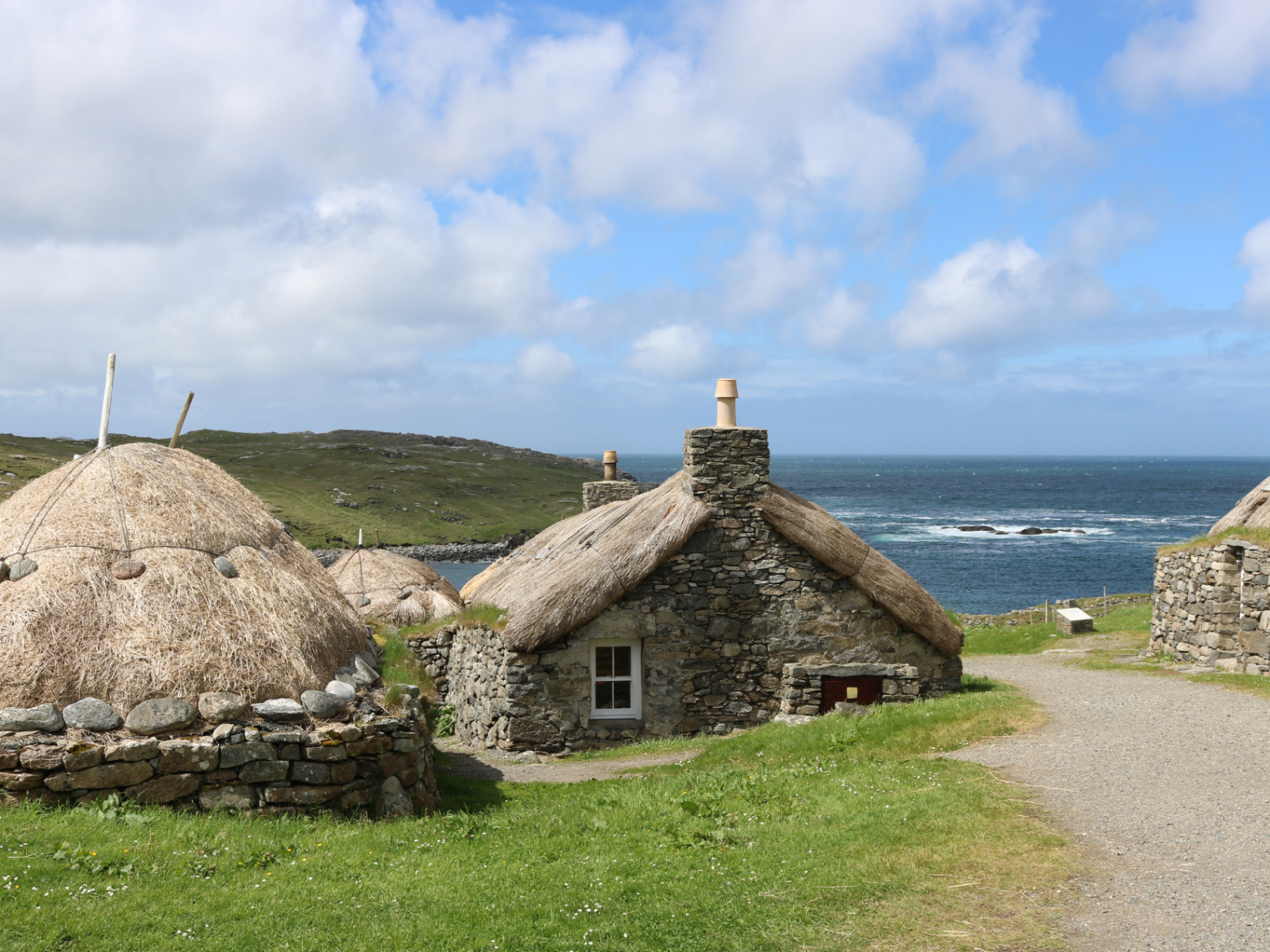 Stone cottages with thatched roofs by sea, cloudy sky above.