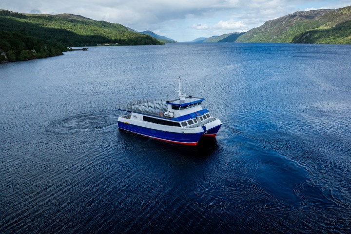 Small tourist boat on a vast, calm lake surrounded by green hills.