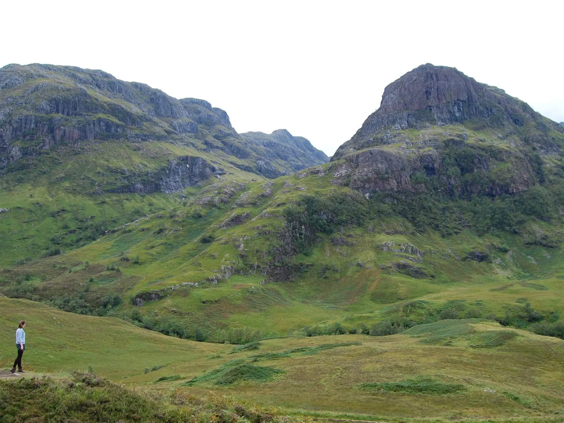 a group of people standing on a lush green hillside with Glen Coe in the background