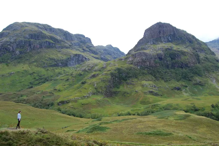a group of people standing on a lush green hillside with Glen Coe in the background