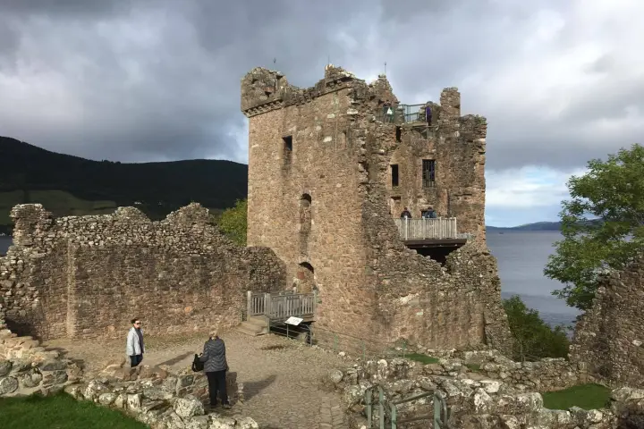 a group of people standing in front of a castle with Urquhart Castle in the background