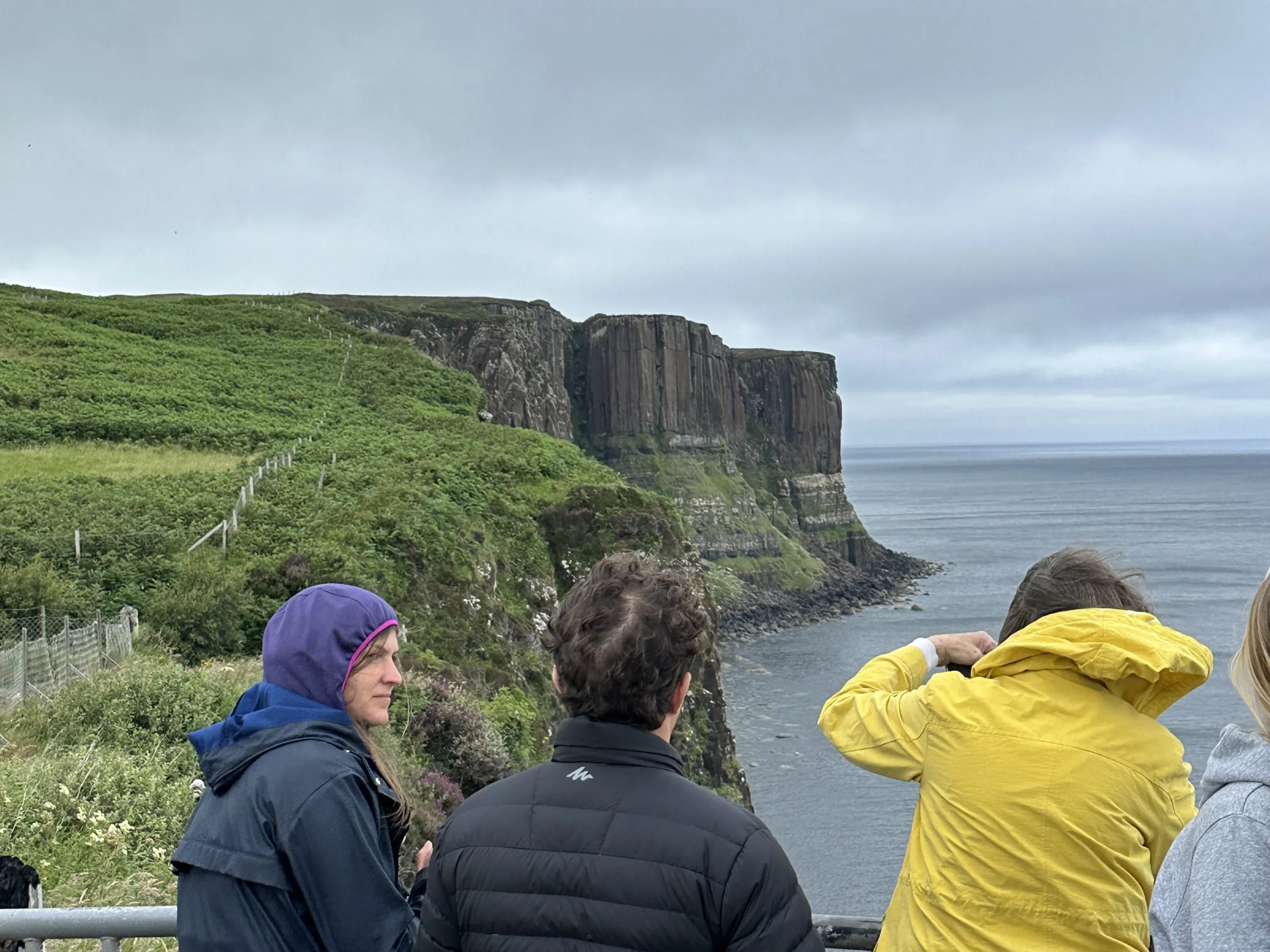 People in jackets viewing a coastal cliff on a cloudy day.