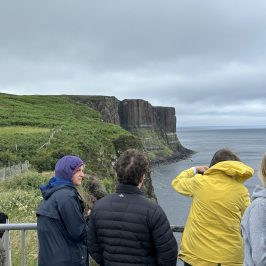 People in jackets viewing a coastal cliff on a cloudy day.