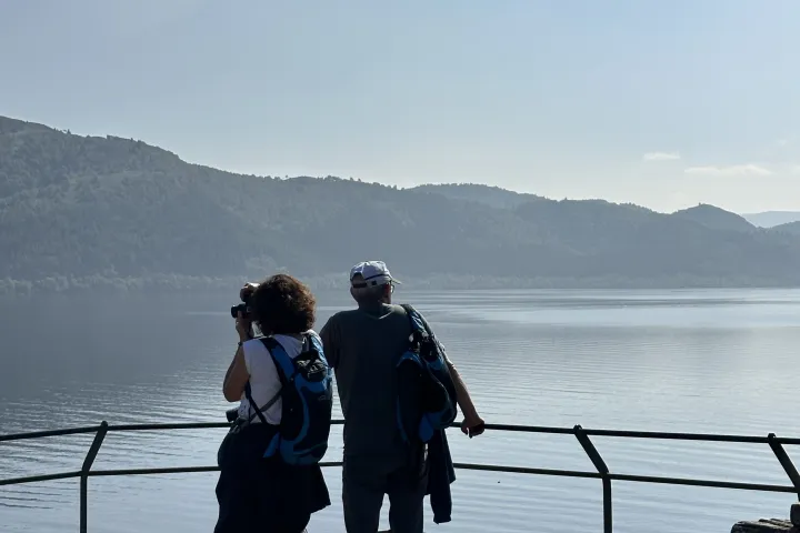 Two people with backpacks overlooking a lake from a railing on a clear day.