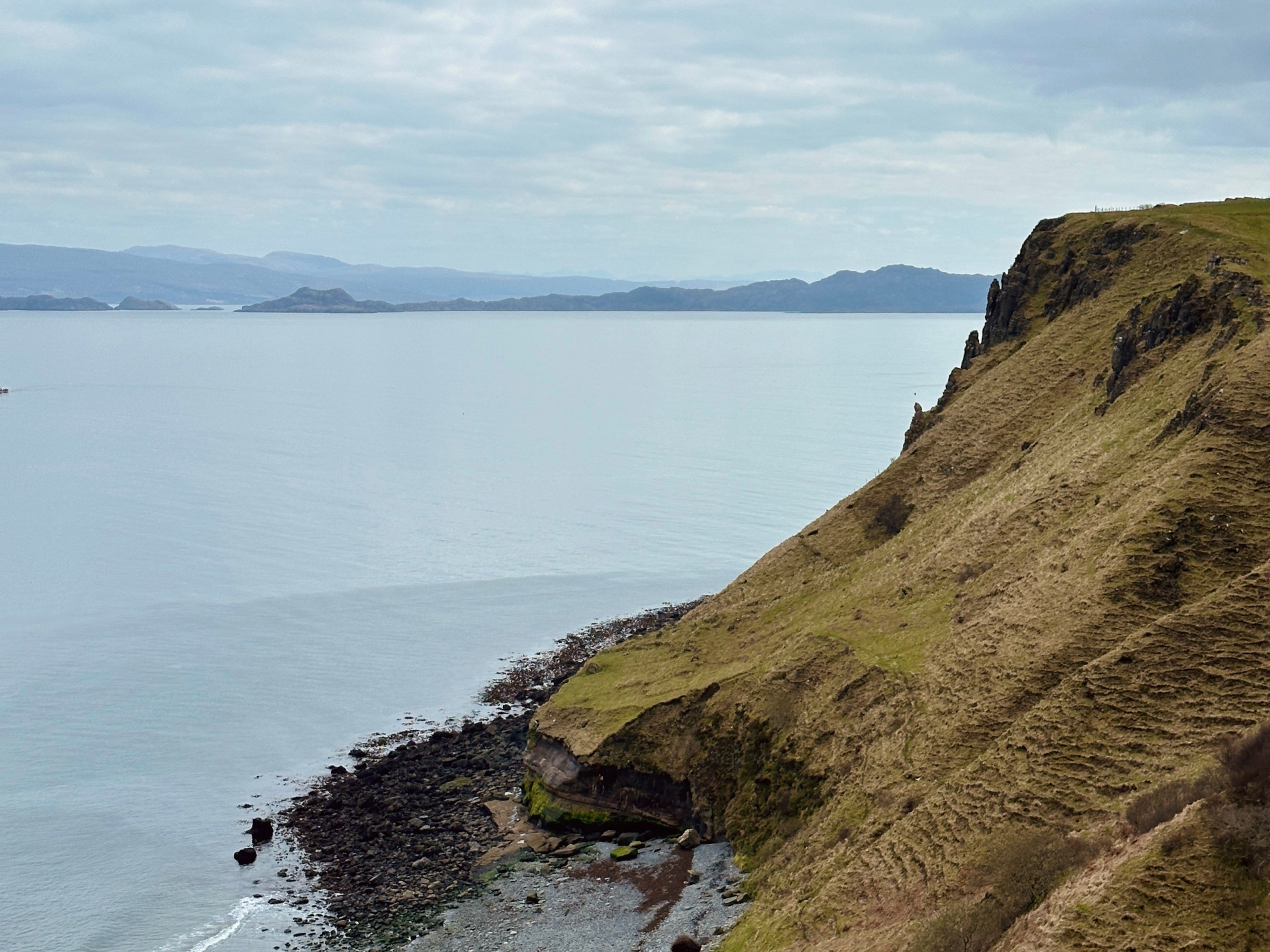 People resting by a cliff overlooking a calm sea and cloudy sky.