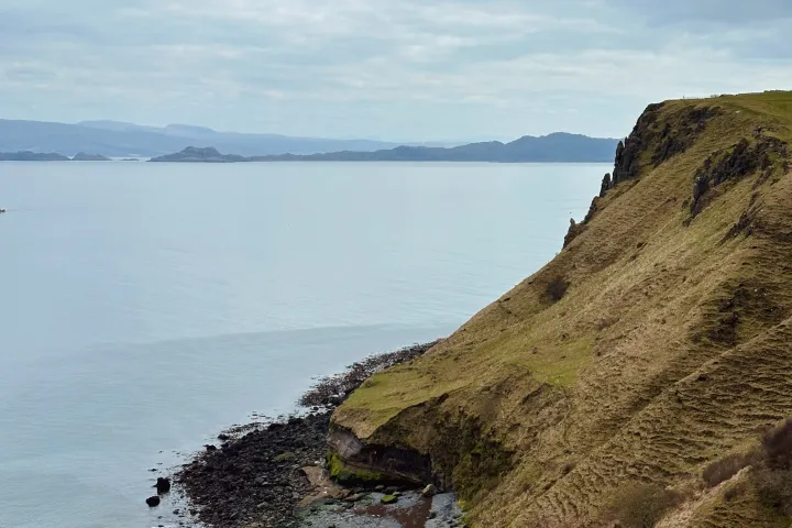 People resting by a cliff overlooking a calm sea and cloudy sky.
