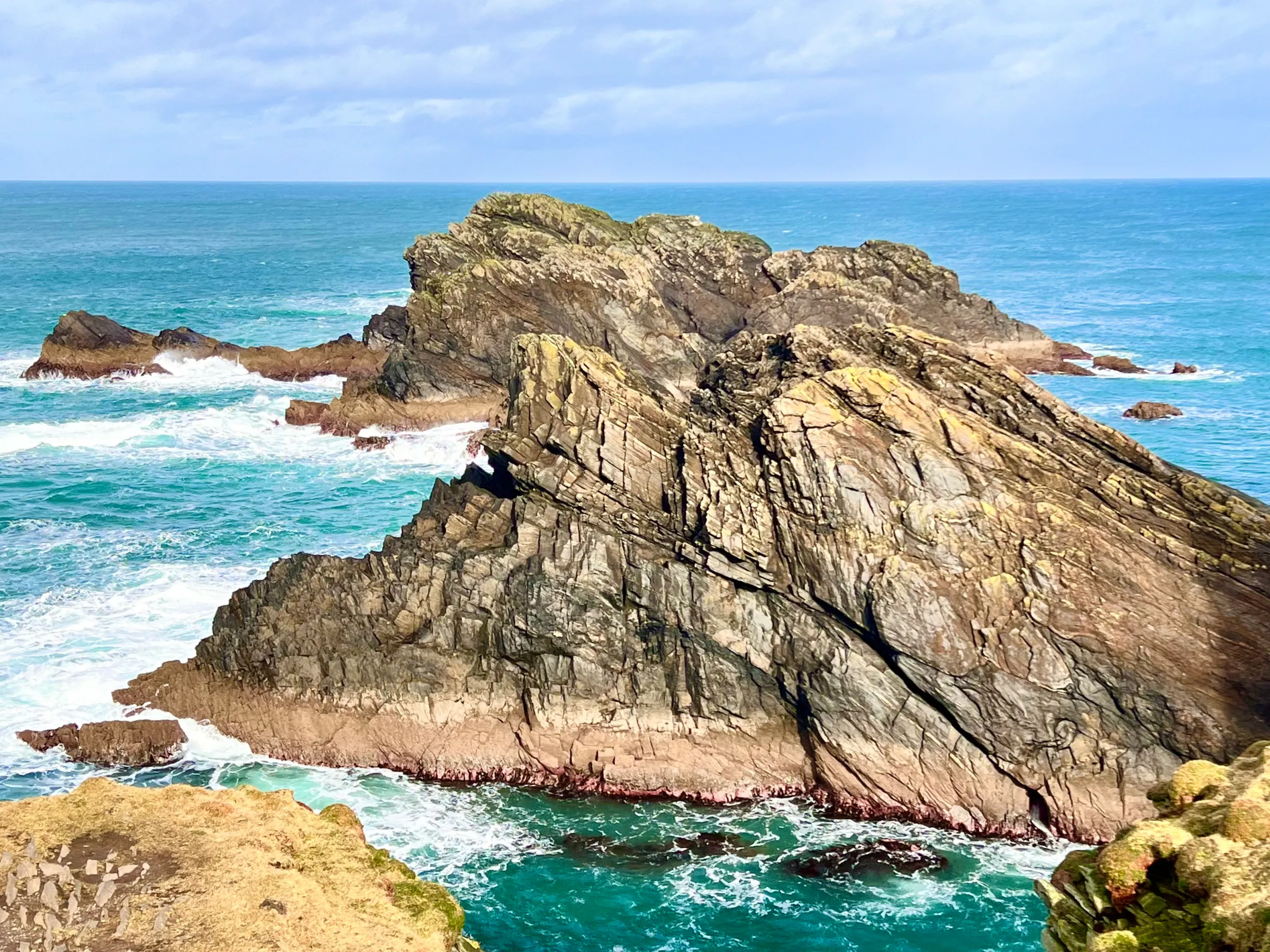 Rocky cliffs and ocean waves under a partly cloudy sky.