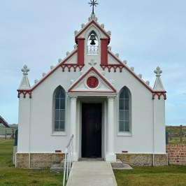 Small white chapel with red trim, pointed roof, bell tower, and arched windows.