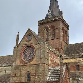 Brick church with a tall steeple and circular stained glass window.
