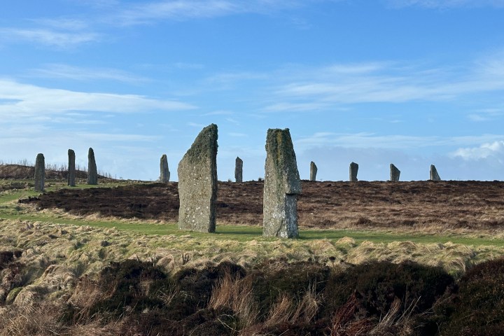 Stone circle with tall, weathered stones under a blue sky.