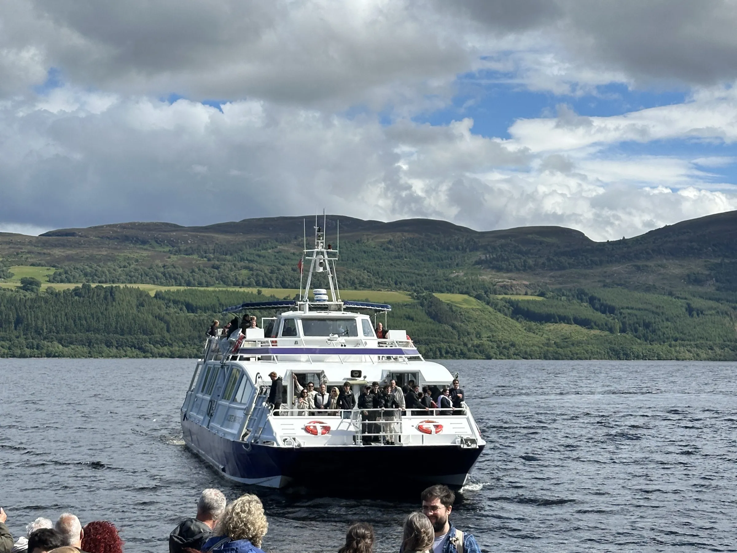 People on boat watching another boat on a lake with hills in the background.