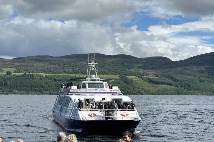 People on boat watching another boat on a lake with hills in the background.