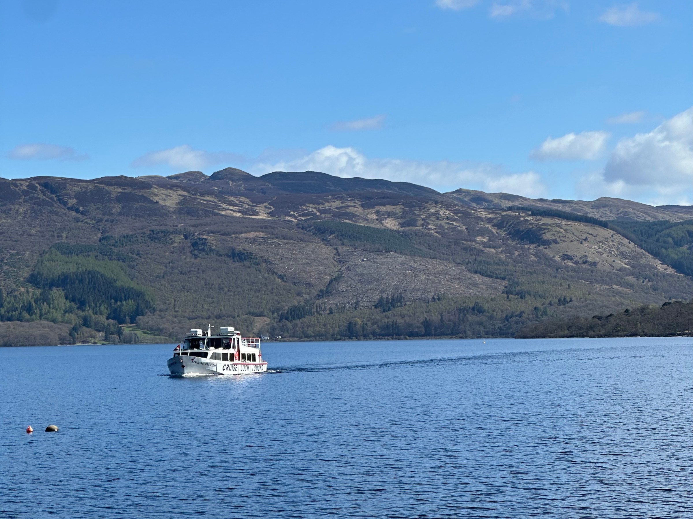 Boat cruising on a lake with mountains in the background under a blue sky.