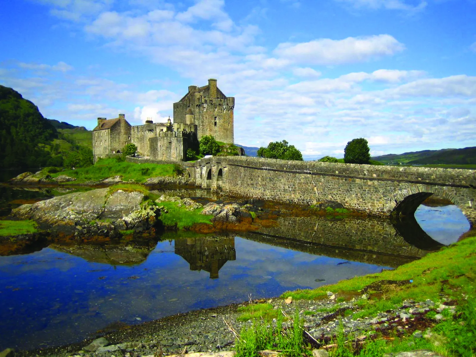 a stone castle next to a body of water with Eilean Donan in the background
