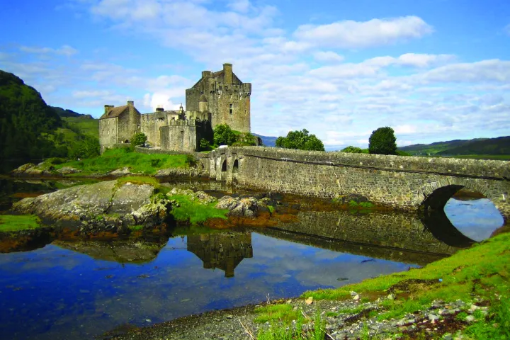 a stone castle next to a body of water with Eilean Donan in the background