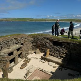 Ancient stone ruins by the sea with tourists overlooking the beach.