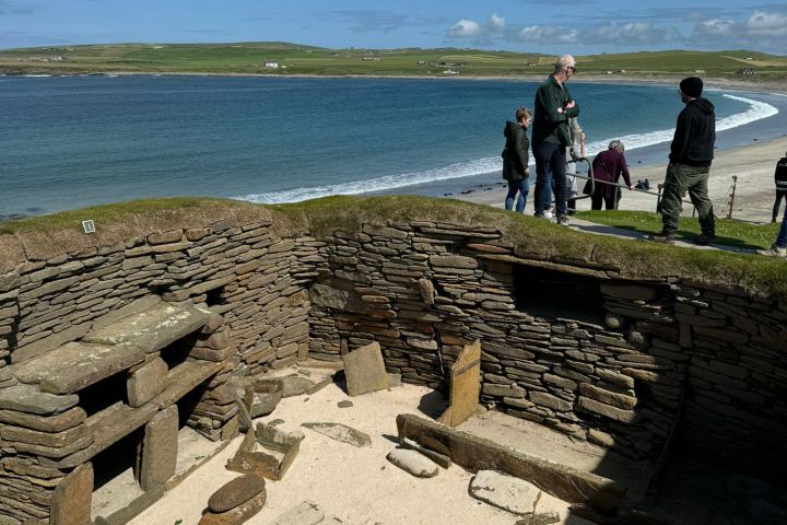 Ancient stone ruins by the sea with tourists overlooking the beach.