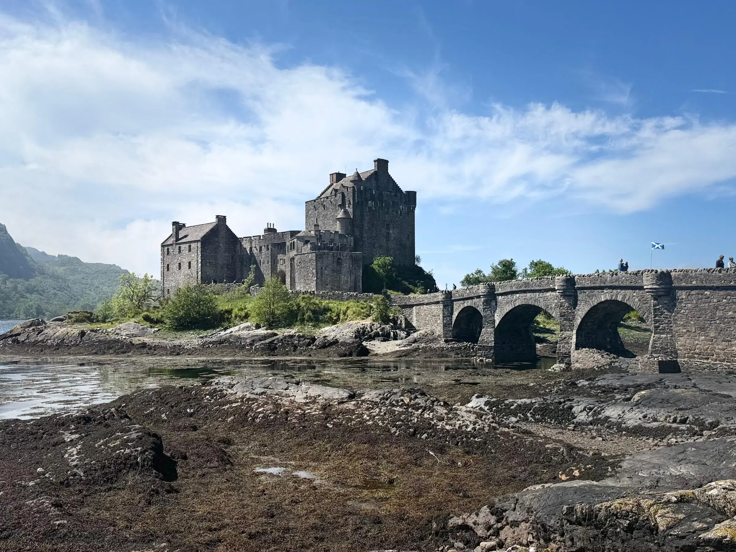 Historic stone castle with bridge over water on a sunny day.