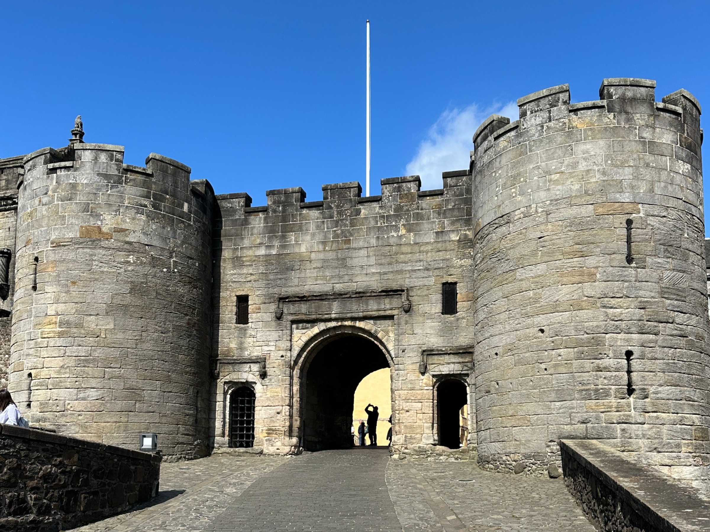 Stone castle entrance with two round towers against a clear blue sky.