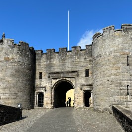 Stone castle entrance with two round towers against a clear blue sky.