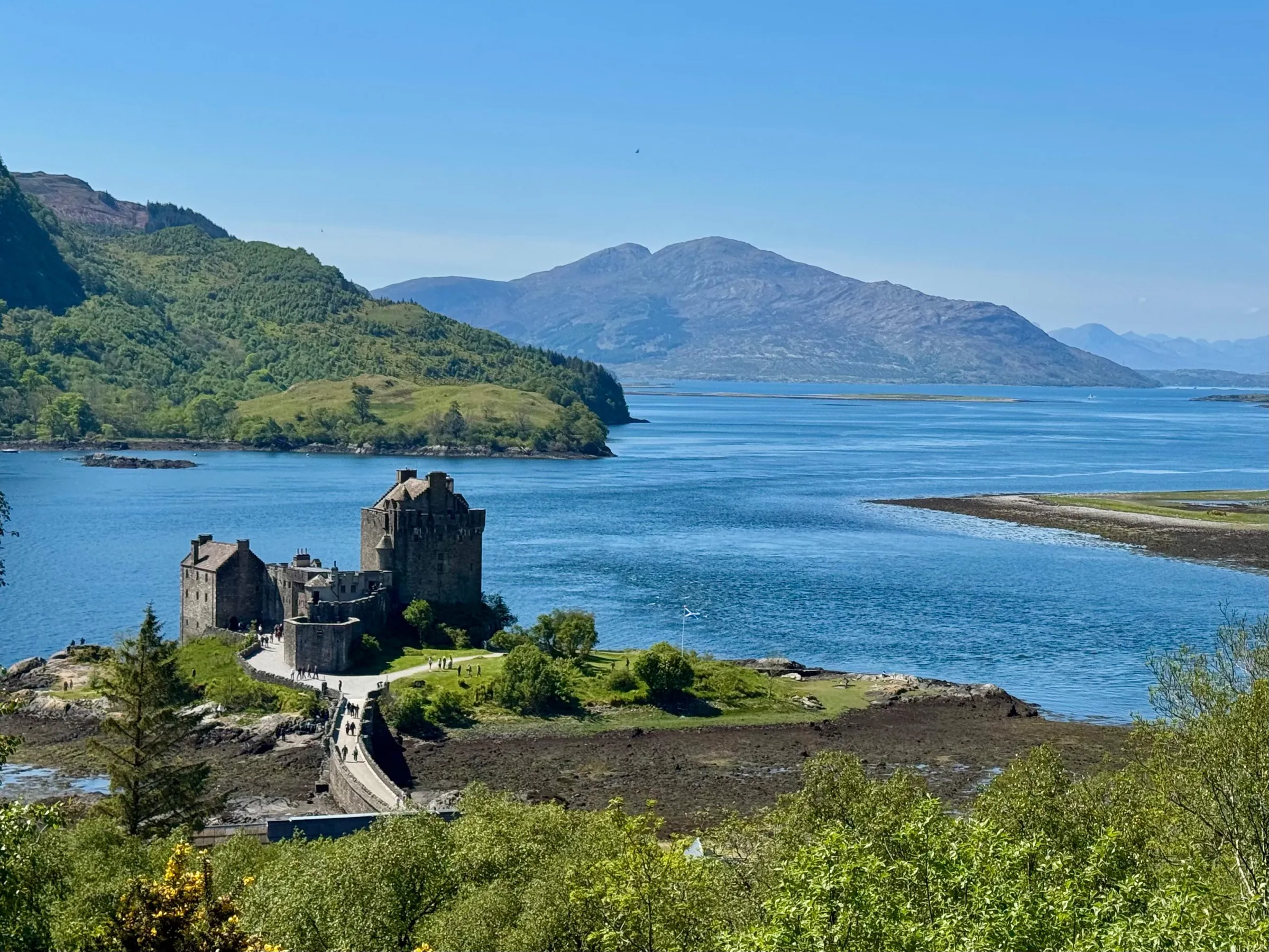 Historic castle on a small island with mountain and water views in sunny weather.