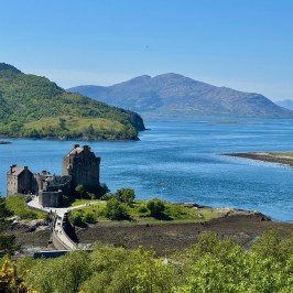 Historic castle on a small island with mountain and water views in sunny weather.