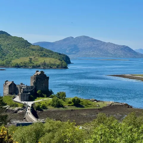 Historic castle on a small island with mountain and water views in sunny weather.
