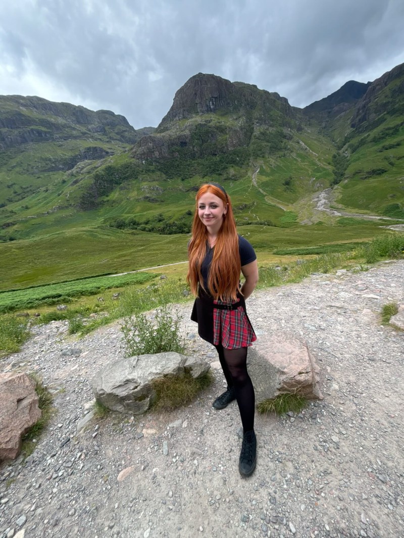 Terri A young lady is standing on the path with green mountains at the back