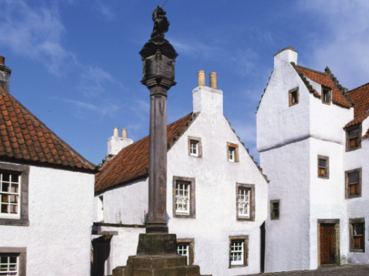Historic white buildings with steep roofs and a stone monument under a blue sky.
