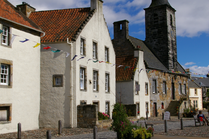 Historic European street with stone buildings, clock tower, and colorful banners.