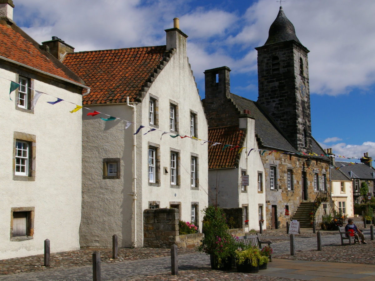Historic stone buildings with flags and a clock tower under a blue sky.