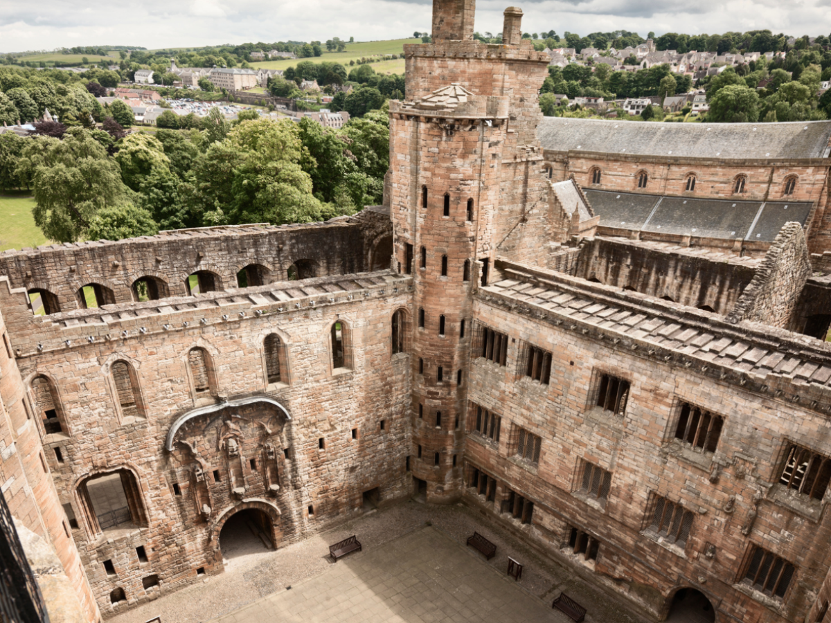 Aerial view of an ancient stone castle with towers, surrounded by greenery.