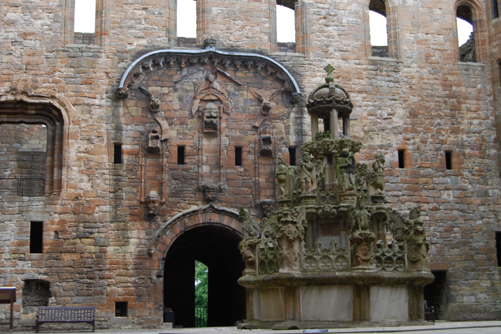 Stone castle courtyard with decorative fountain and arched entrance.