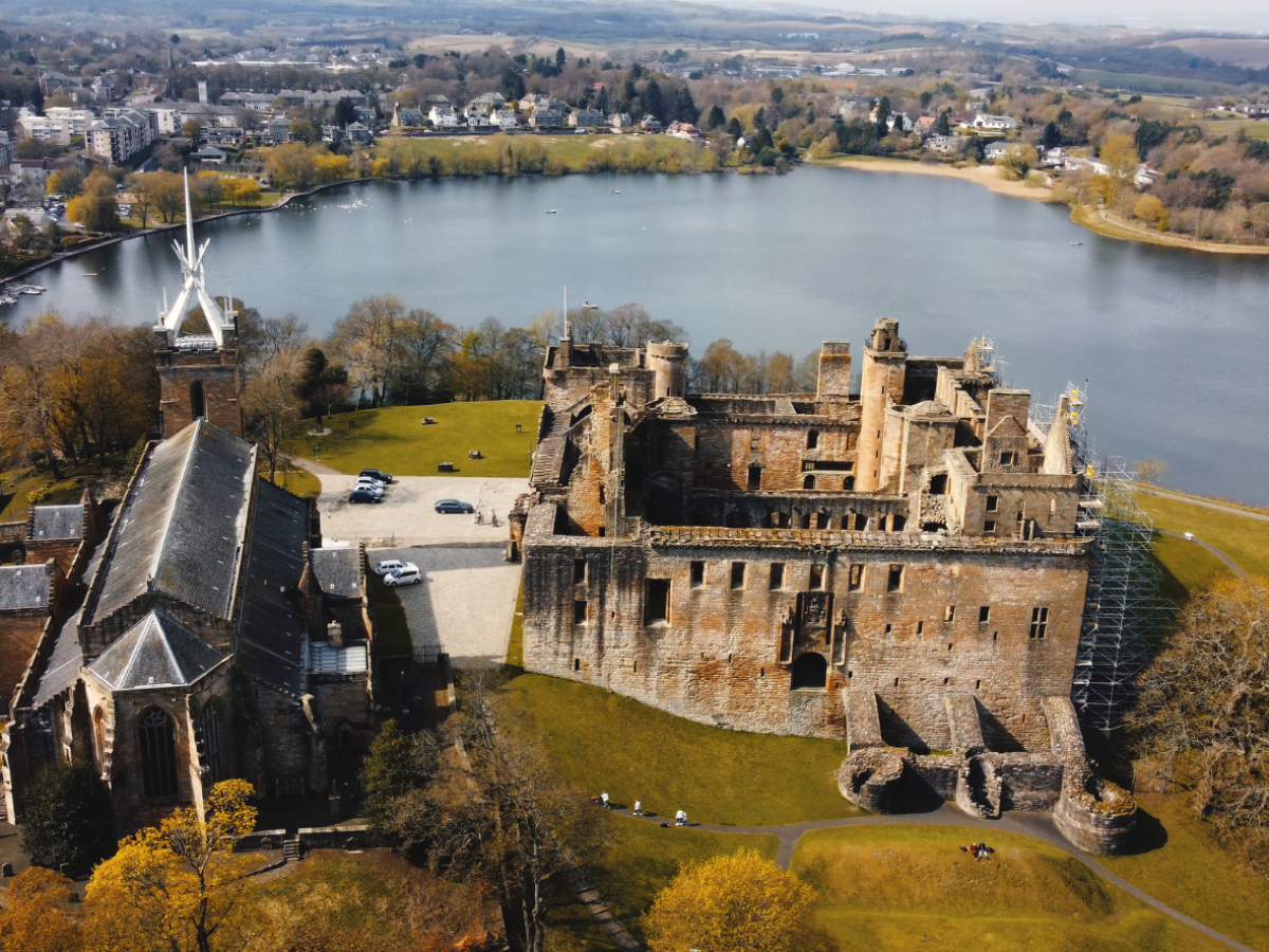 Aerial view of a historical castle and church by a large lake with a town in the background.