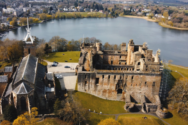 Aerial view of a historical castle and church by a large lake with a town in the background.
