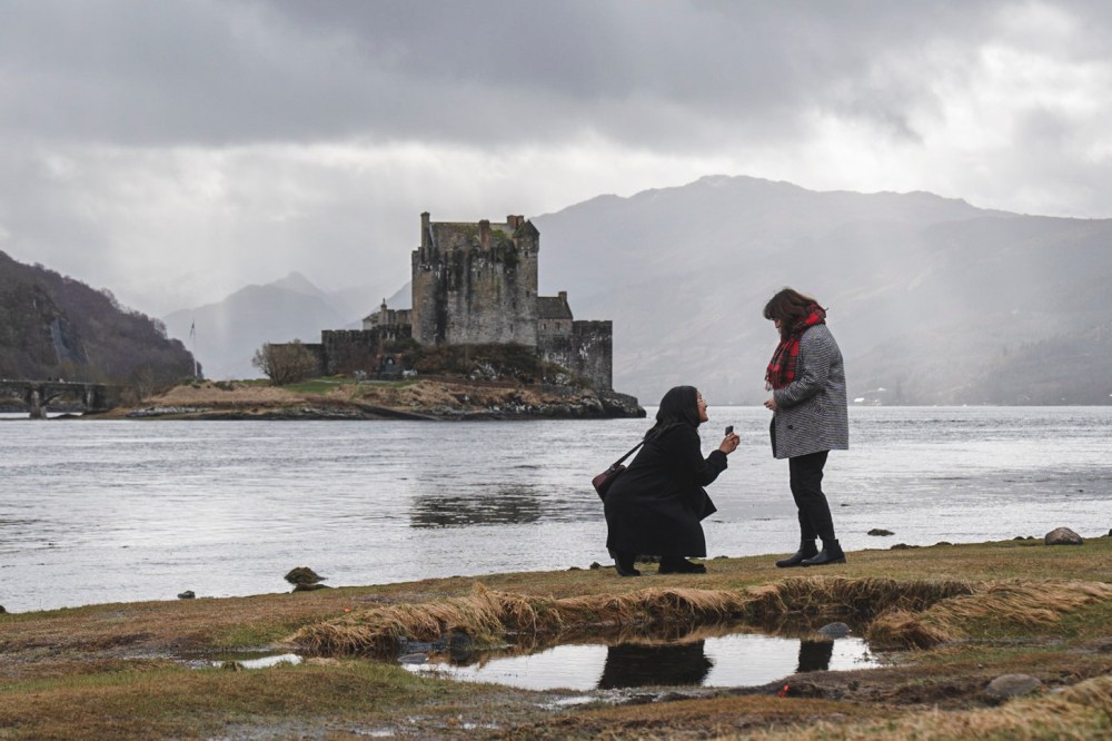 a man standing next to a body of water with Eilean Donan in the background