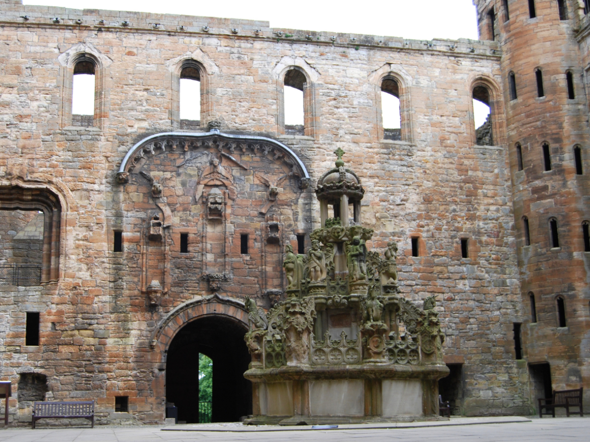Stone castle courtyard with intricate fountain and archway.