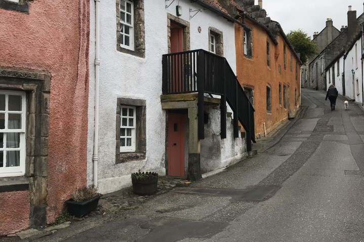 Historic street with colorful houses and cobblestone sidewalk under a cloudy sky.