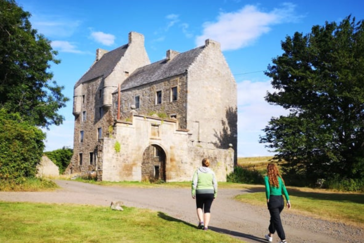 Two people walking toward an old stone building under a blue sky.