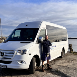 Man standing beside a white van near a harbor with boats.