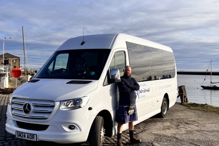 Man standing beside a white van near a harbor with boats.