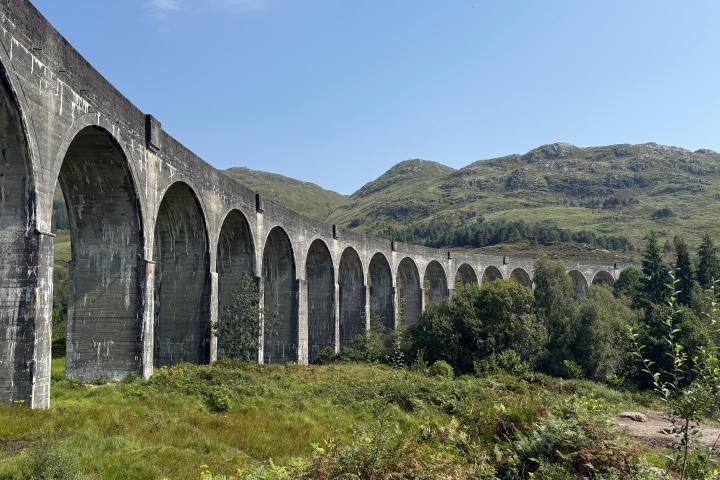 Stone viaduct with multiple arches spanning a lush, green landscape.