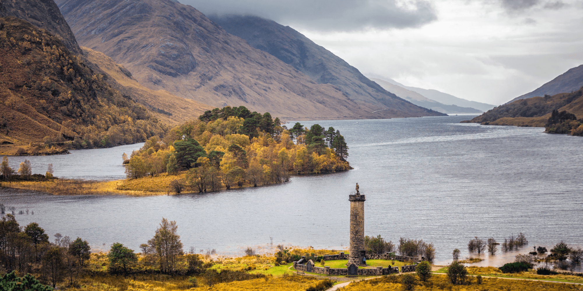 Scenic view of a lake with a monument on shore, surrounded by hills.