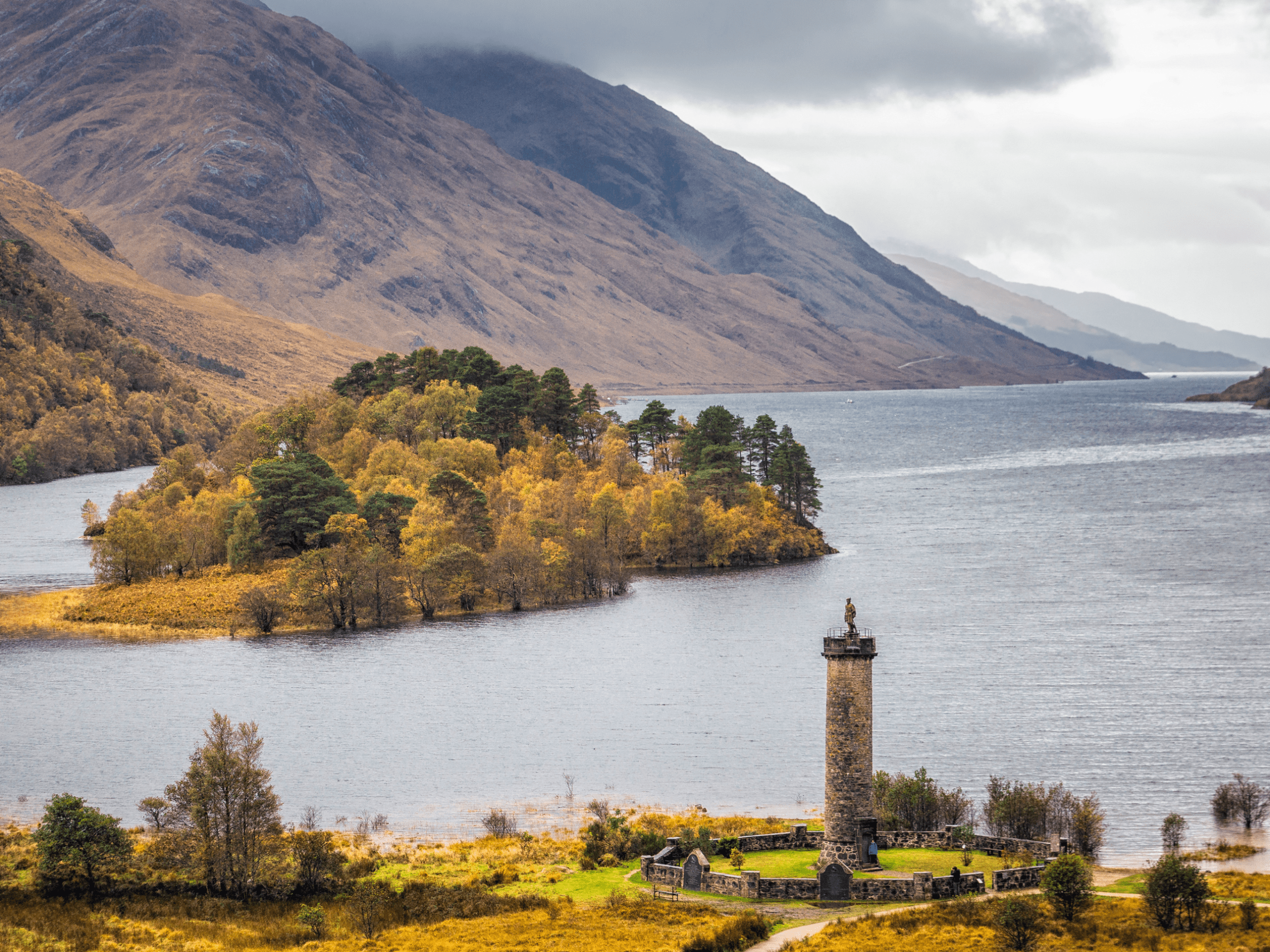 Scenic view of a lake with a monument on shore, surrounded by hills.
