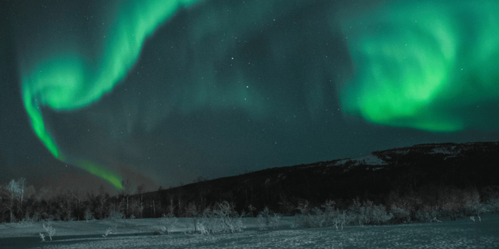 Vibrant green aurora borealis lighting up the night sky over a snowy landscape.