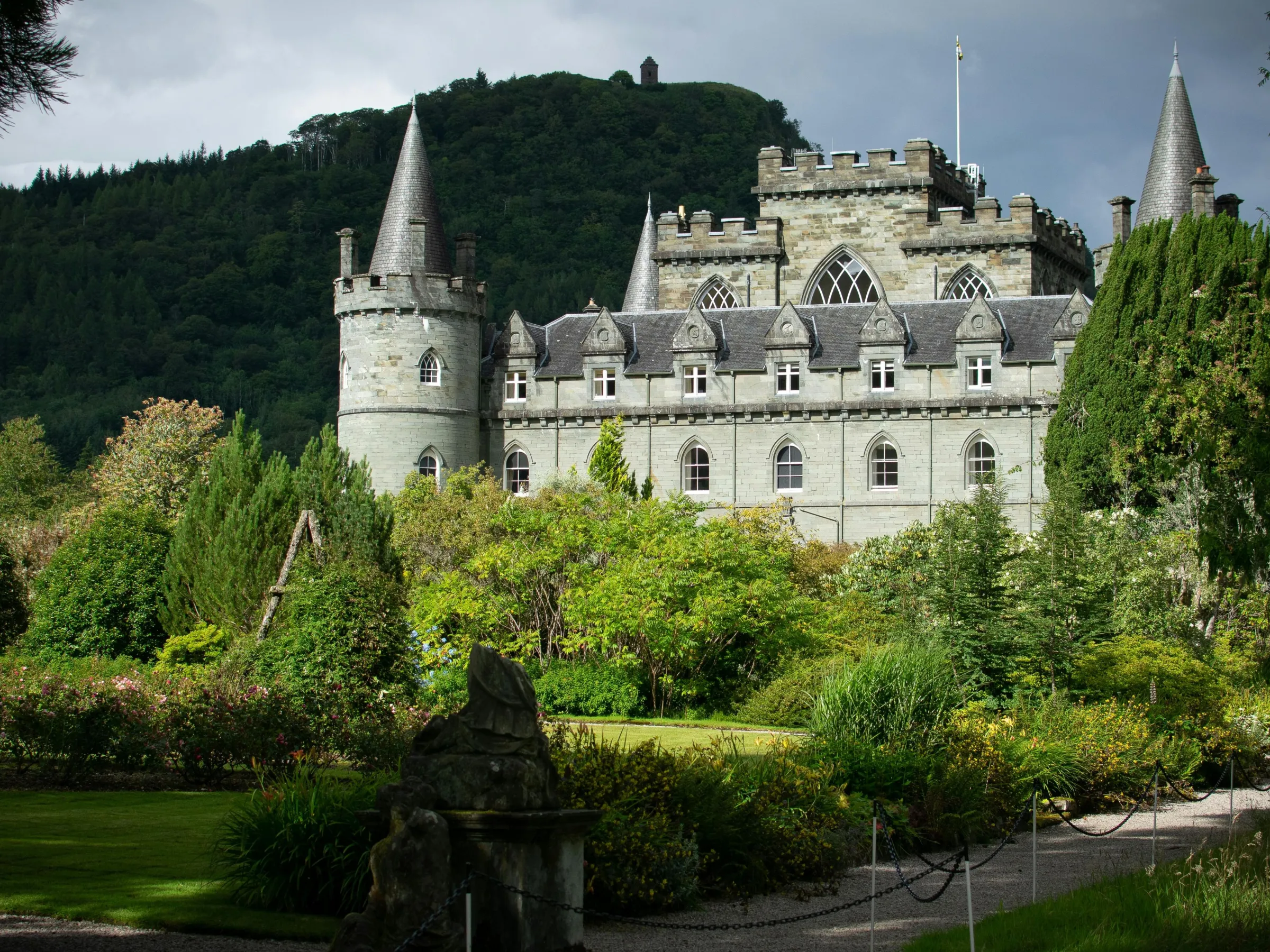 A historic stone castle with towers surrounded by lush greenery under a cloudy sky.