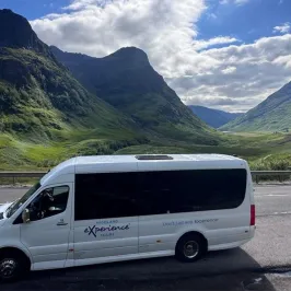 White tour bus on a road with mountainous landscape and cloudy sky in the background.